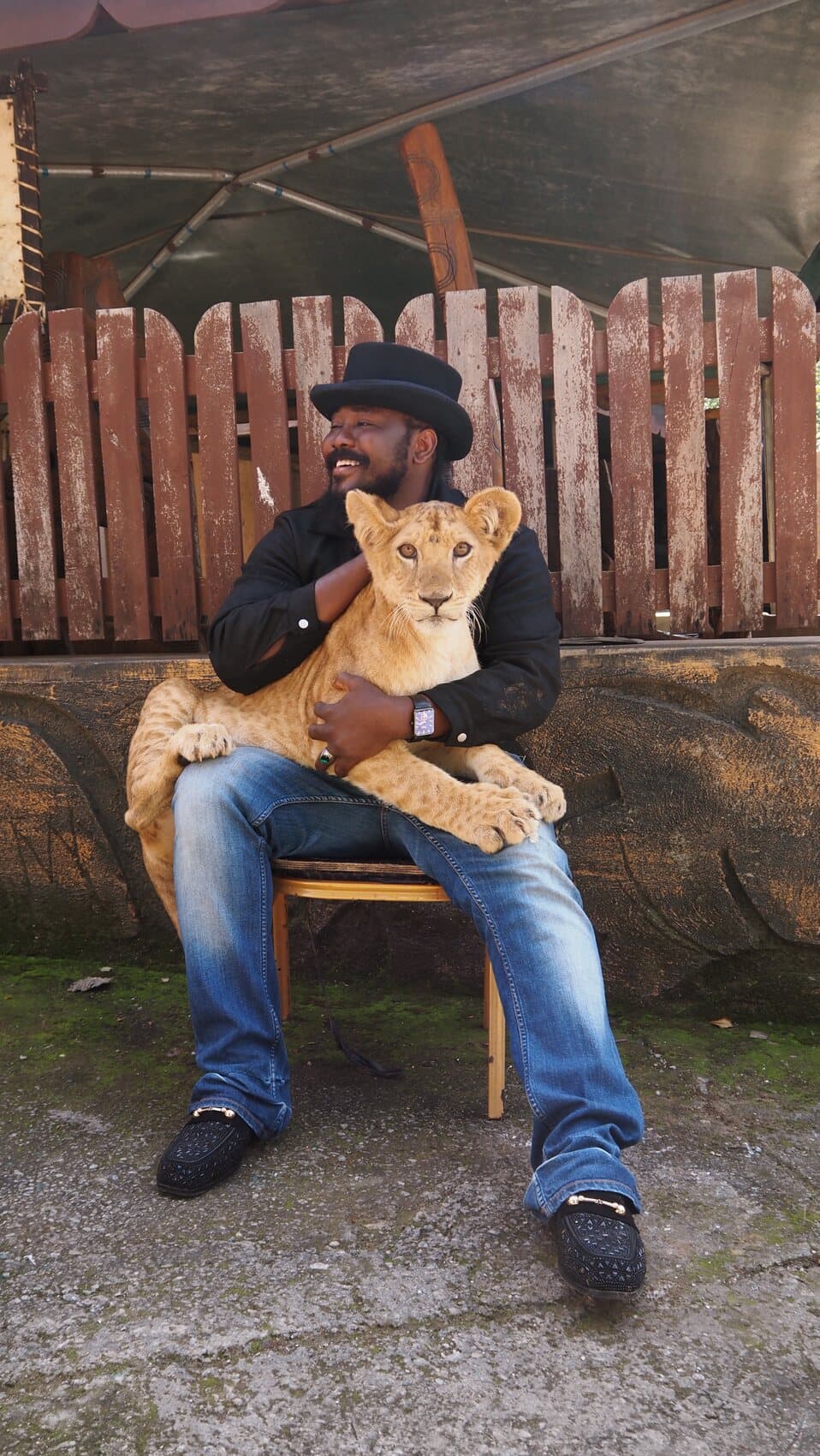 ABJKOREA laughing with a lion cub in his arms, wearing a black top hat.