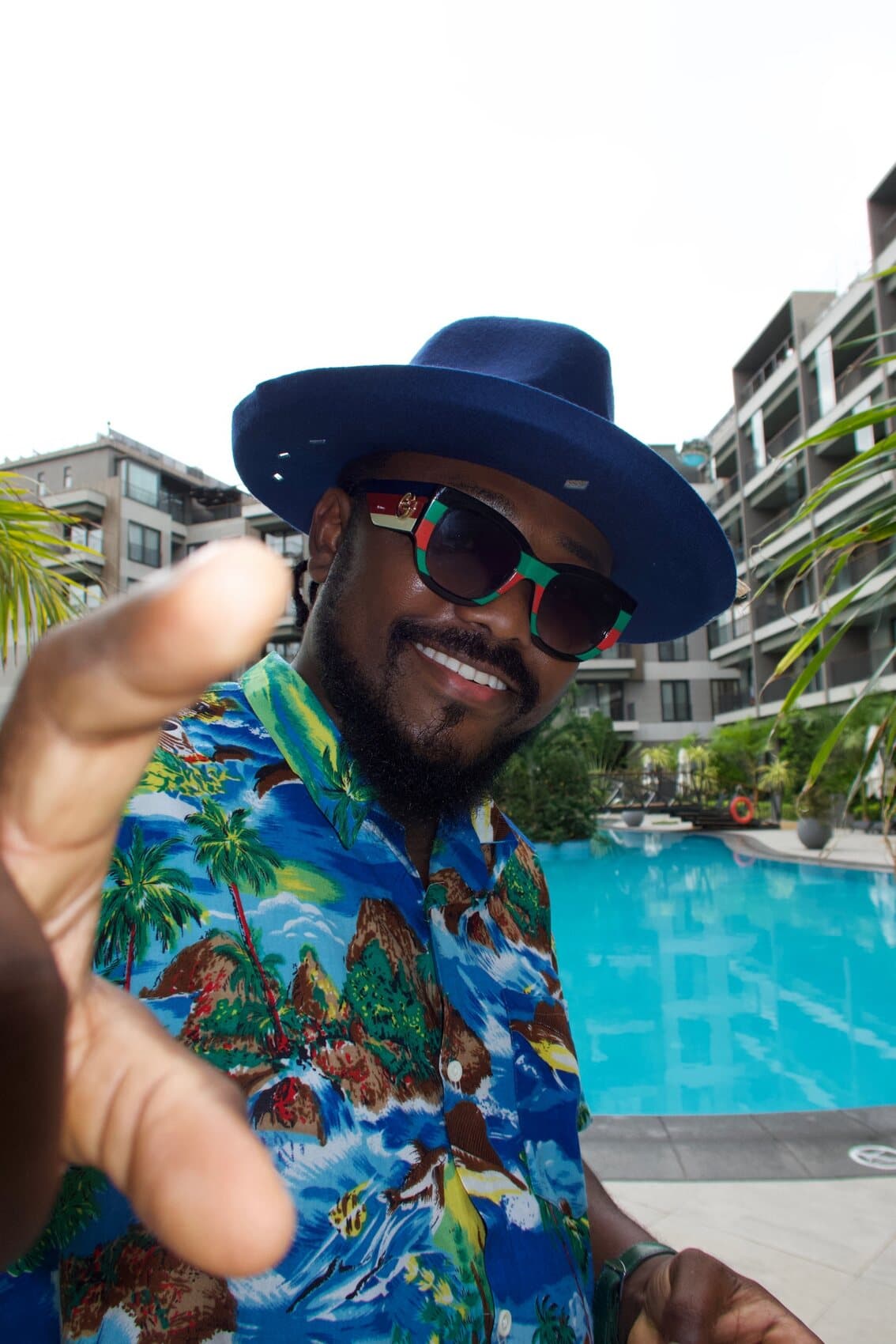 ABJKOREA poolside in a blue fedora, patterned shirt and green-striped sunglasses.