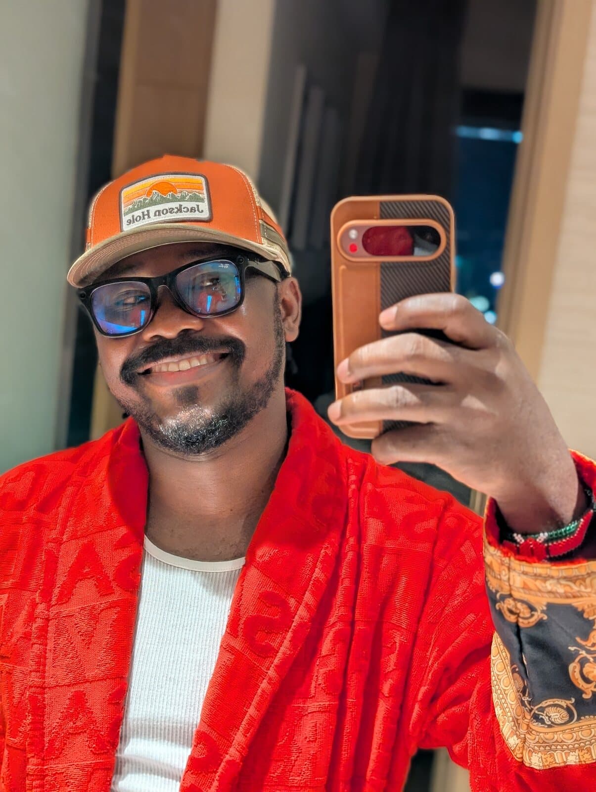 Mirror self-portrait of ABJKOREA in a red robe and trucker cap, phone in hand.